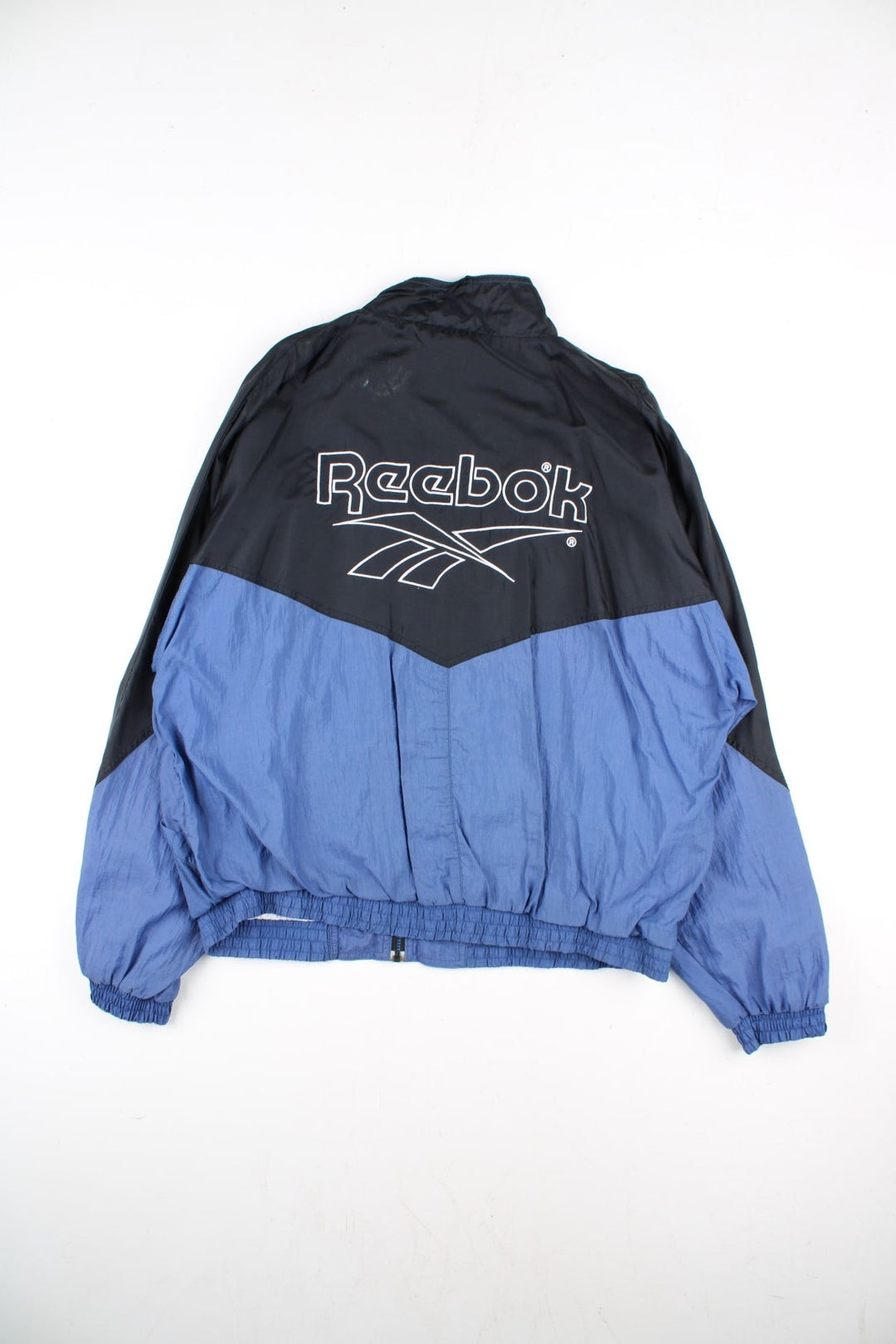 Vintage Reebok Track Top in a black colourway with blue bottom half panelling. Full zip with two side pockets and large reebok logo on the back.