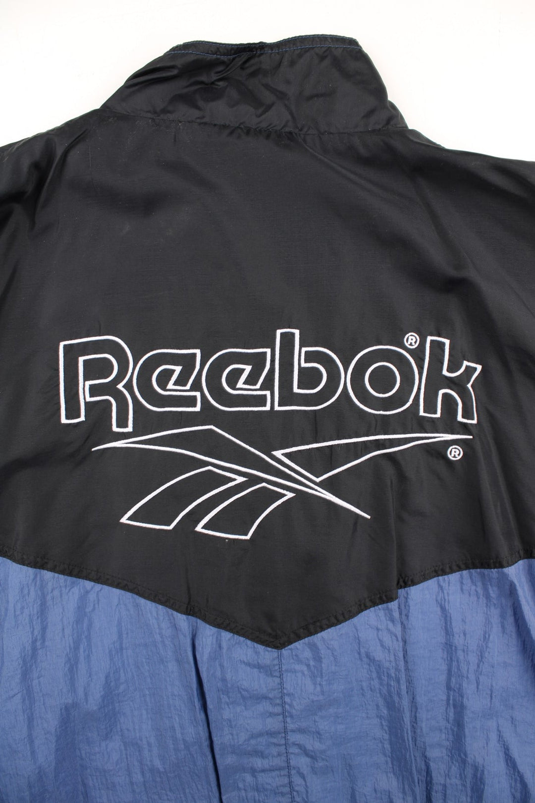 Vintage Reebok Track Top in a black colourway with blue bottom half panelling. Full zip with two side pockets and large reebok logo on the back.