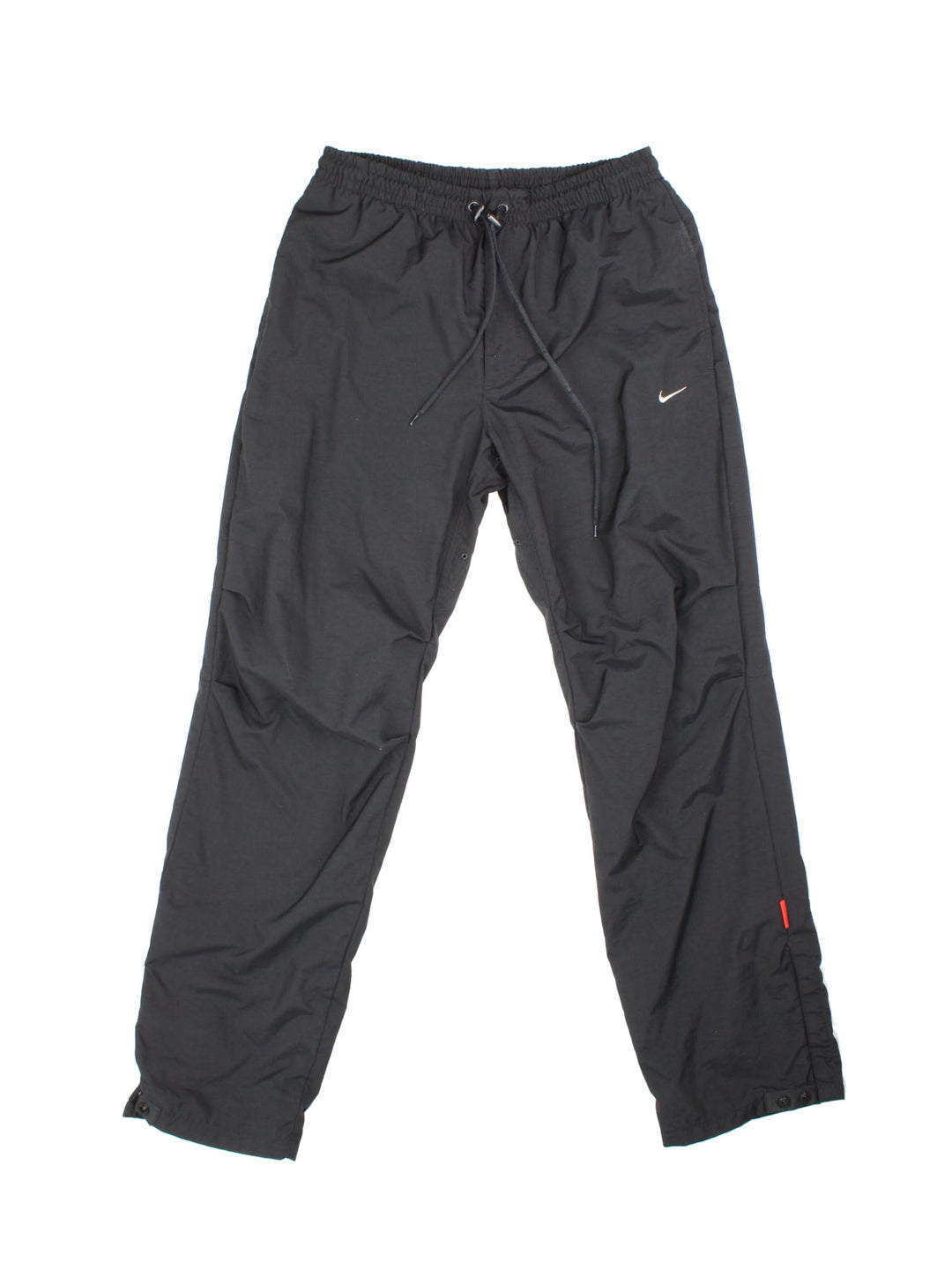 Nike tracksuit bottoms in black with four pockets, a drawstring at the waist, snap-open cuffs and an embroidered swoosh in white.