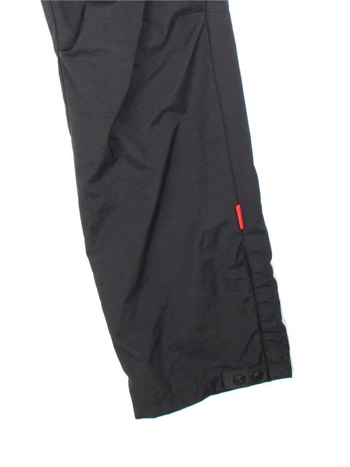 Nike tracksuit bottoms in black with four pockets, a drawstring at the waist, snap-open cuffs and an embroidered swoosh in white.