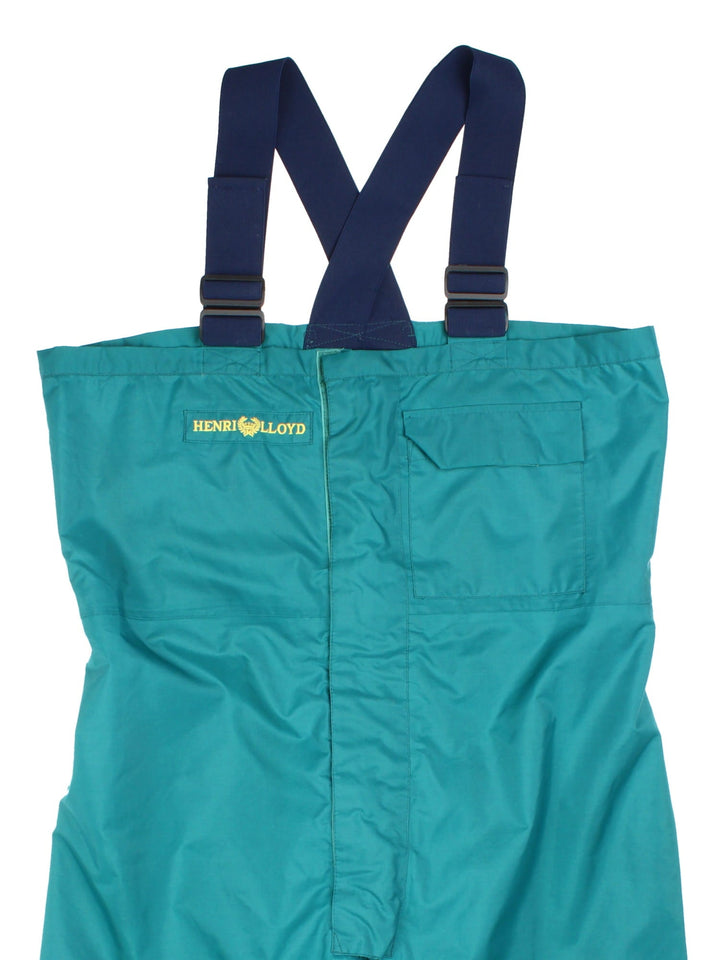 Vintage Henri lloyd Hi-Fit Offshore salopettes in blue with two pockets, zip and velcro closure, adjustable braces, velcro tighteners at the cuffs, and an embroidered logo on the front in yellow.