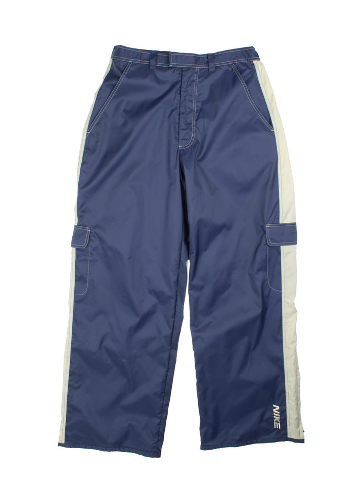 Nike tracksuit bottoms in navy blue with grey stripe detailing, multiple pockets, white contrast stitching, embroidered logos and zip, snap and button closure.