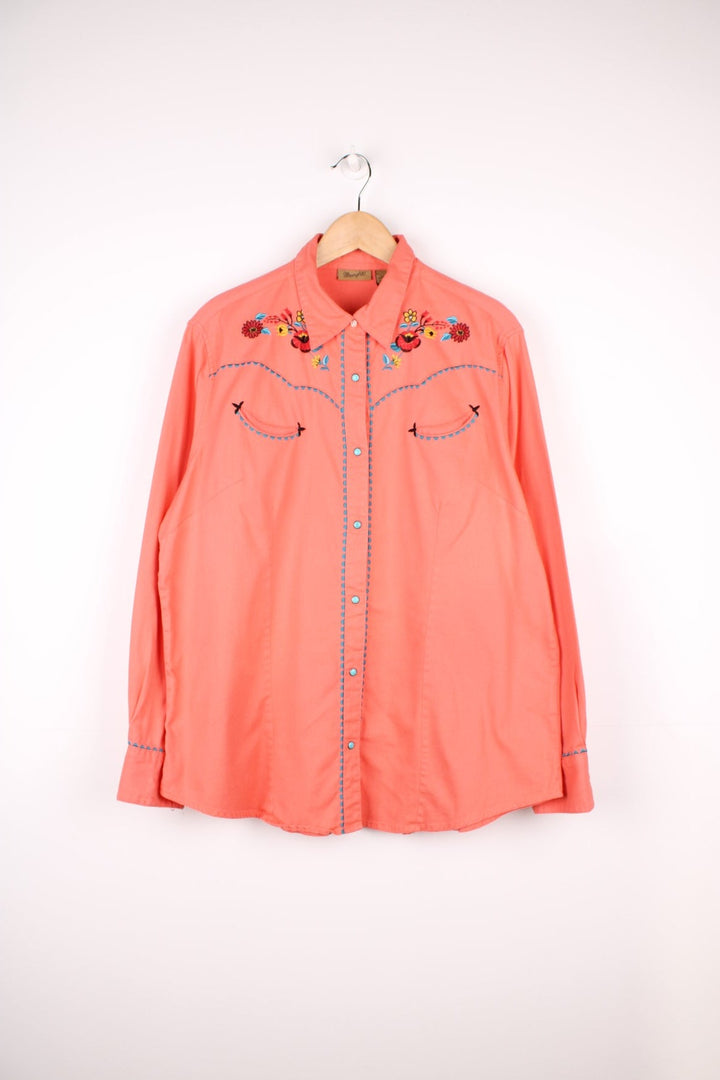 Pink Wrangler western shirt with floral embroidery on yoke, pockets and cuffs, a ram's skull embroidered on the back, and turqoise-effect snap closure. 