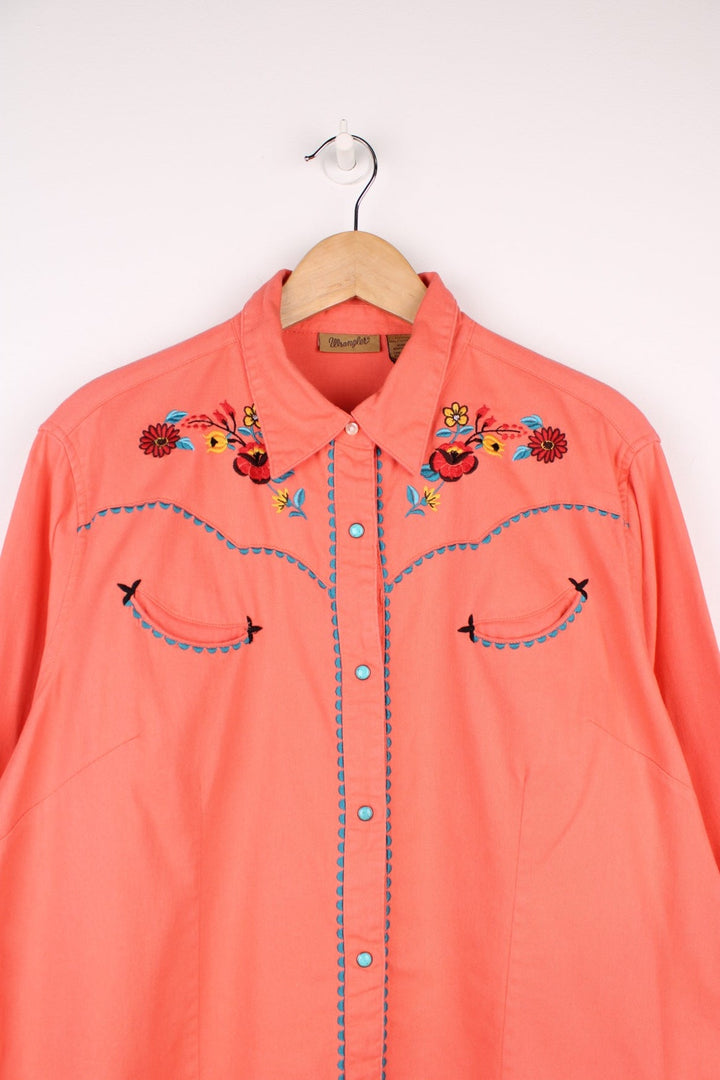 Pink Wrangler western shirt with floral embroidery on yoke, pockets and cuffs, a ram's skull embroidered on the back, and turqoise-effect snap closure. 