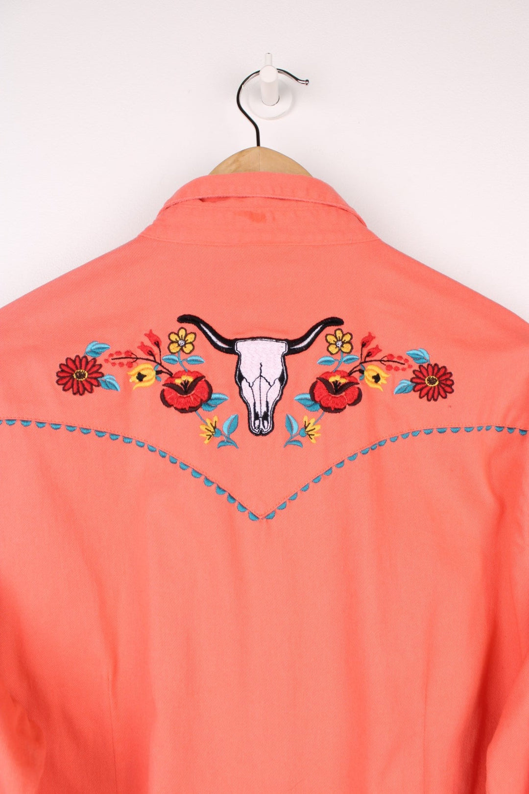 Pink Wrangler western shirt with floral embroidery on yoke, pockets and cuffs, a ram's skull embroidered on the back, and turqoise-effect snap closure. 