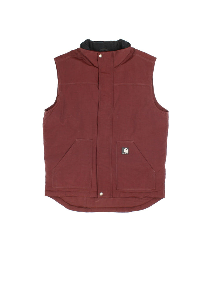 Carhartt Gilet in a burgundy red colourway. Zips up and has side pockets, insulated with a quilted lining, and has the logo embroidered on the front.