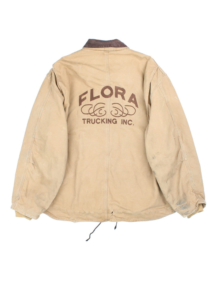 Vintage Carhartt Arctic Jacket in a tan colourway. Zips up and has multiple pockets, insulated with a sherpa lining, has the logo embroidered on the front, and 'Flora Trucking Inc' company logo / spell out embroidered on the back.