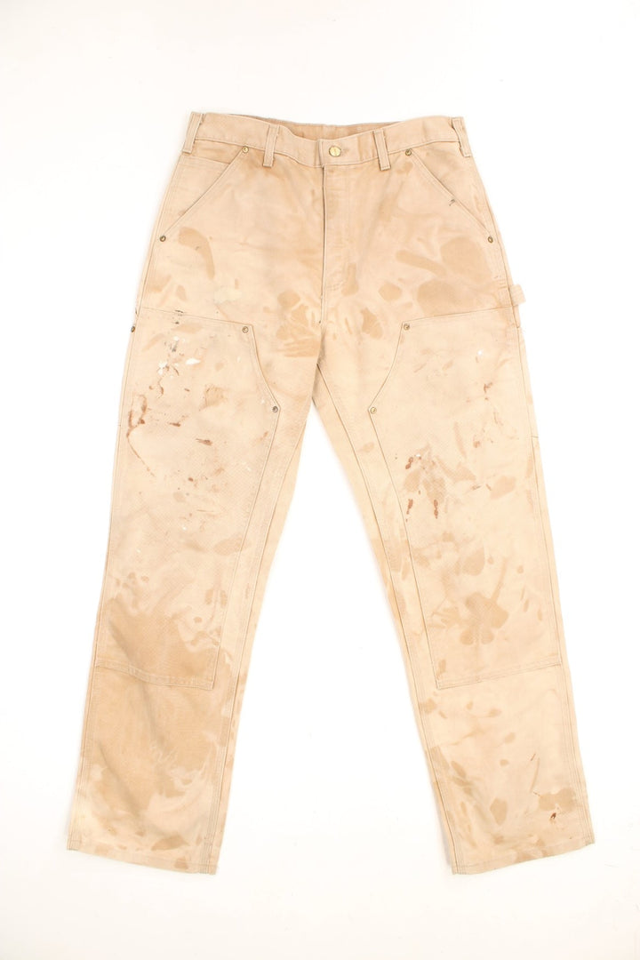 Carhartt Carpenter Jeans in a tanned colourway with paint marks throughout, dungaree fit, multiple pockets and has the logo embroidered on the back. 