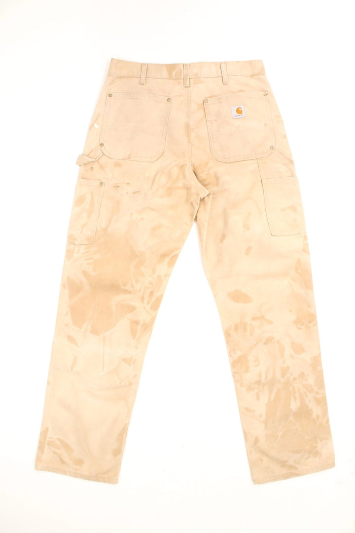 Carhartt Carpenter Jeans in a tanned colourway with paint marks throughout, dungaree fit, multiple pockets and has the logo embroidered on the back. 