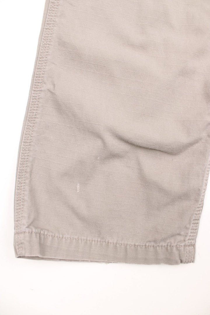 Carhartt grey-beige trousers with front, back and side pockets and a logo patch on the back pocket. 