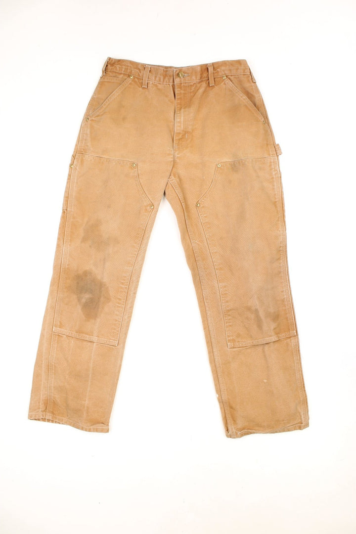 Carhartt tan double knee jeans with a hammer loop, front, back and side pockets and a logo patch on the back pocket. 