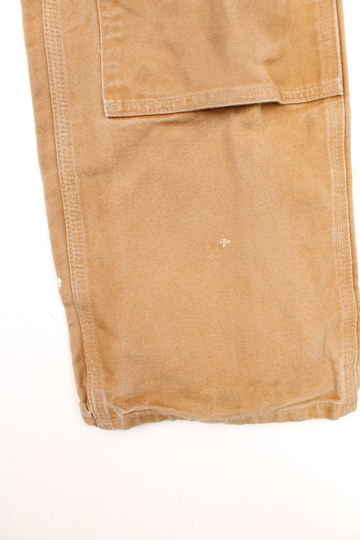 Carhartt tan double knee jeans with a hammer loop, front, back and side pockets and a logo patch on the back pocket. 