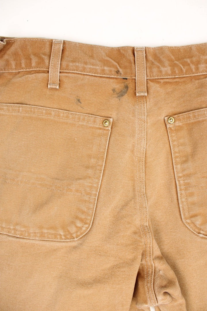 Carhartt tan double knee jeans with a hammer loop, front, back and side pockets and a logo patch on the back pocket. 