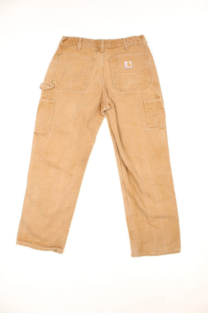 Carhartt tan double knee jeans with a hammer loop, front, back and side pockets and a logo patch on the back pocket. 