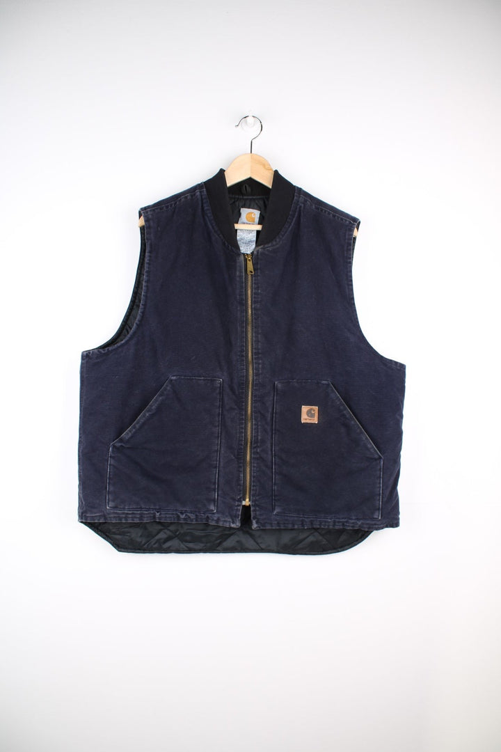 Carhartt Gilet Jacket in an indigo blue colourway. The gilet has two front pockets, a metal zippper to close, and the Carhartt leather patch stitched onto the pocket. 