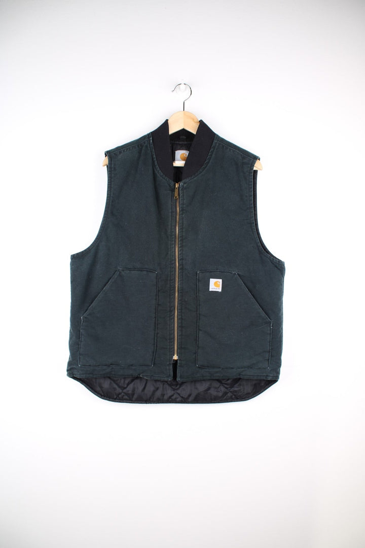 Carhartt Gilet Jacket in a dark green colourway. The gilet has two front pockets, a metal zip to close and the Carhartt logo stitched onto the front.  