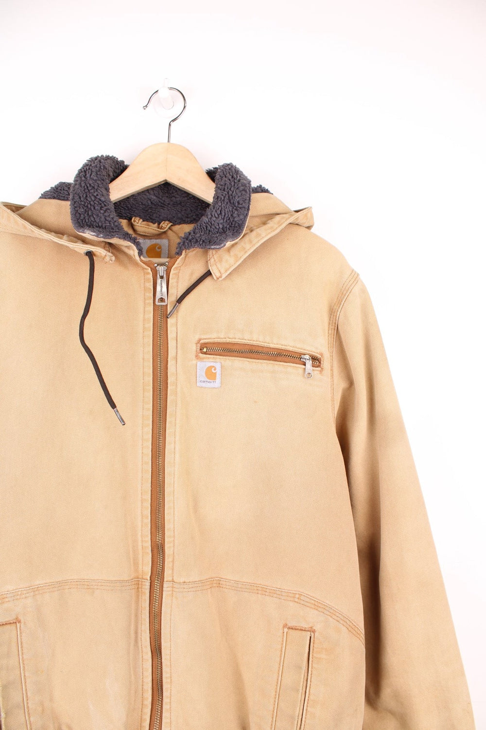 Carhartt Wildwood Sherpa Jacket in tan with zip closure, multiple pockets, sherpa lining, detachable hood and the logo embroidered on the front. 