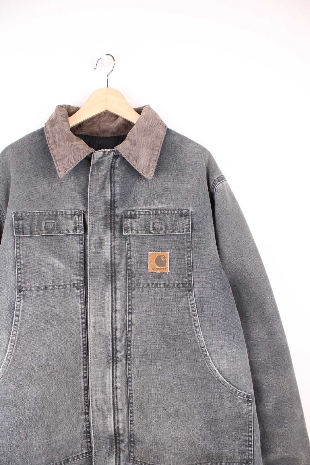 Grey Carhartt Arctic jacket. Quilt lined with a brown corduroy collar, double breast flap pockets and double side pockets, zip and velcro closure, and a brown leather logo patch. 