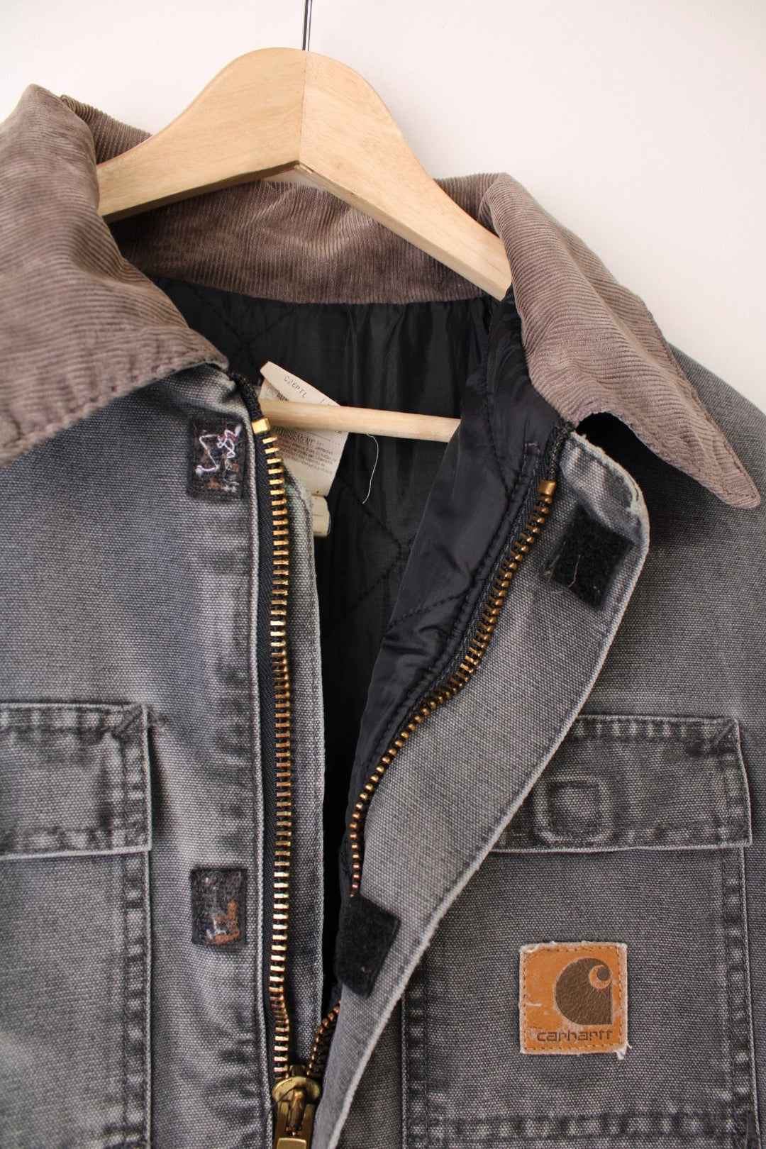 Grey Carhartt Arctic jacket. Quilt lined with a brown corduroy collar, double breast flap pockets and double side pockets, zip and velcro closure, and a brown leather logo patch. 