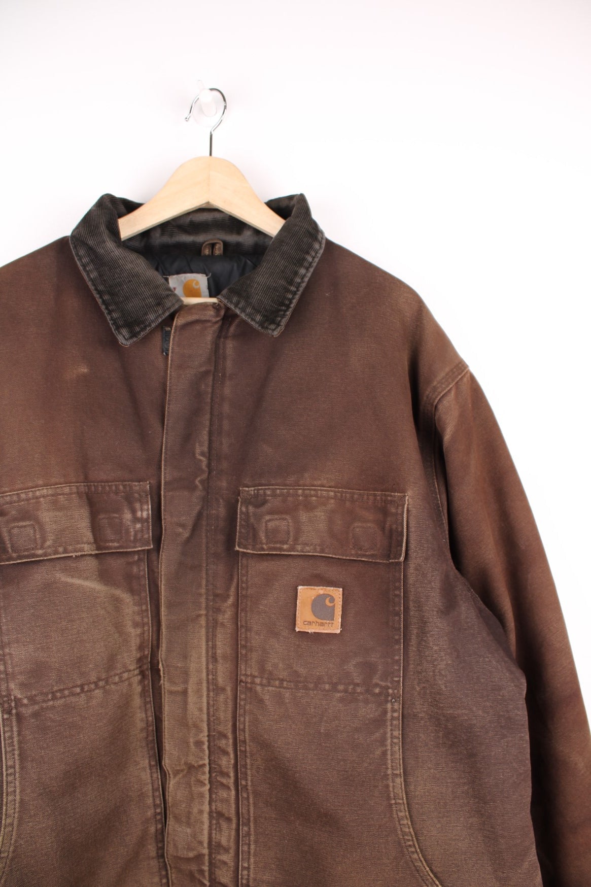 Carhartt Arctic jacket in brown. Quilt lined, with a dark brown corduroy collar,zip and velcro closure, four pockets and a leather logo patch on the upper left.  