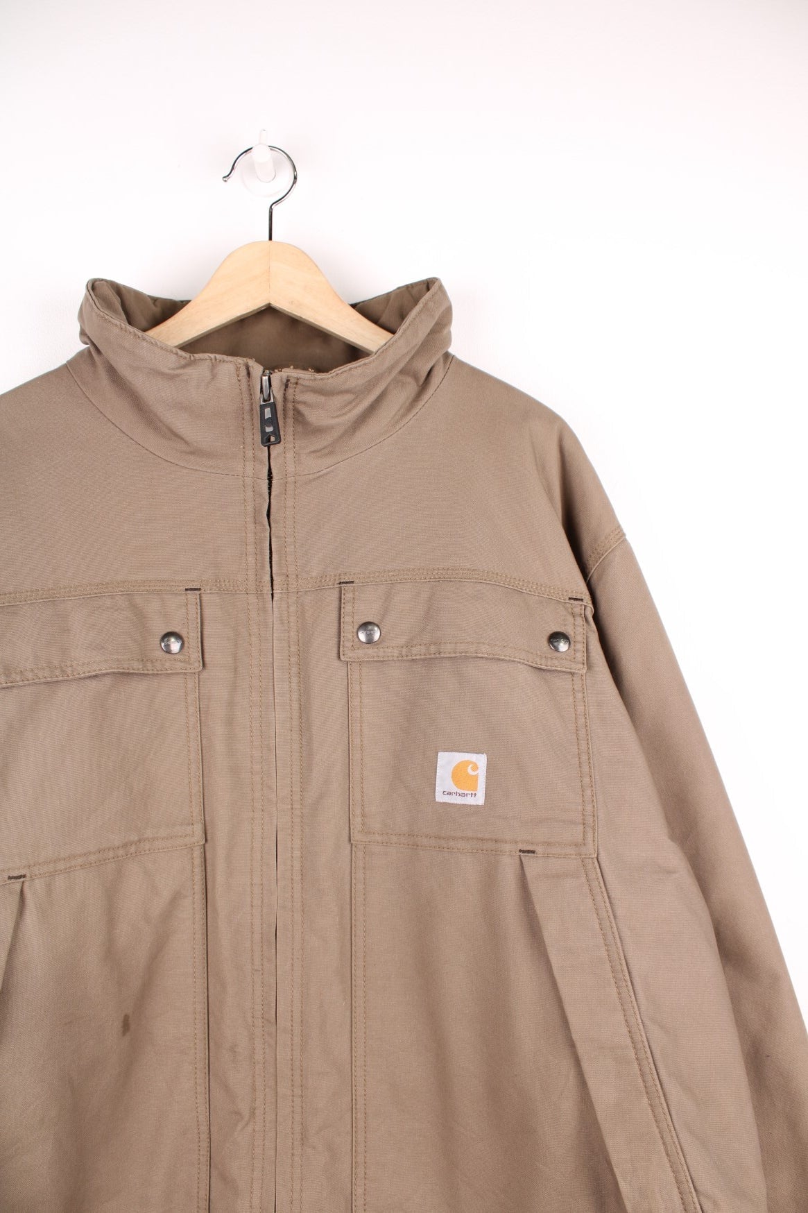 Carhartt work jacket in tan with four pockets, zip closure, a Carhartt logo patch on the upper left and a &