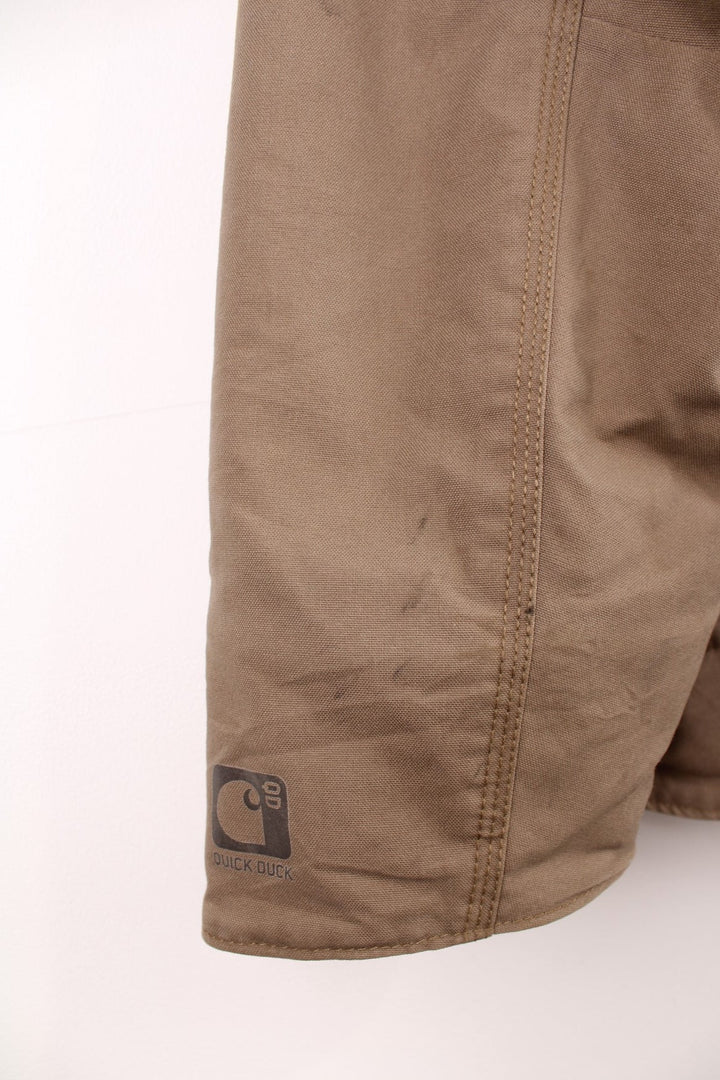 Carhartt work jacket in tan with four pockets, zip closure, a Carhartt logo patch on the upper left and a 'QD Quick Duck' logo on the left sleeve. 