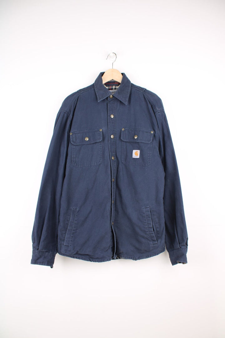 Carhartt Shirt Jacket in a navy blue colourway, heavy cotton material, button up with multiple pockets, has a tartan lining, and the logo embroidered on the front. 