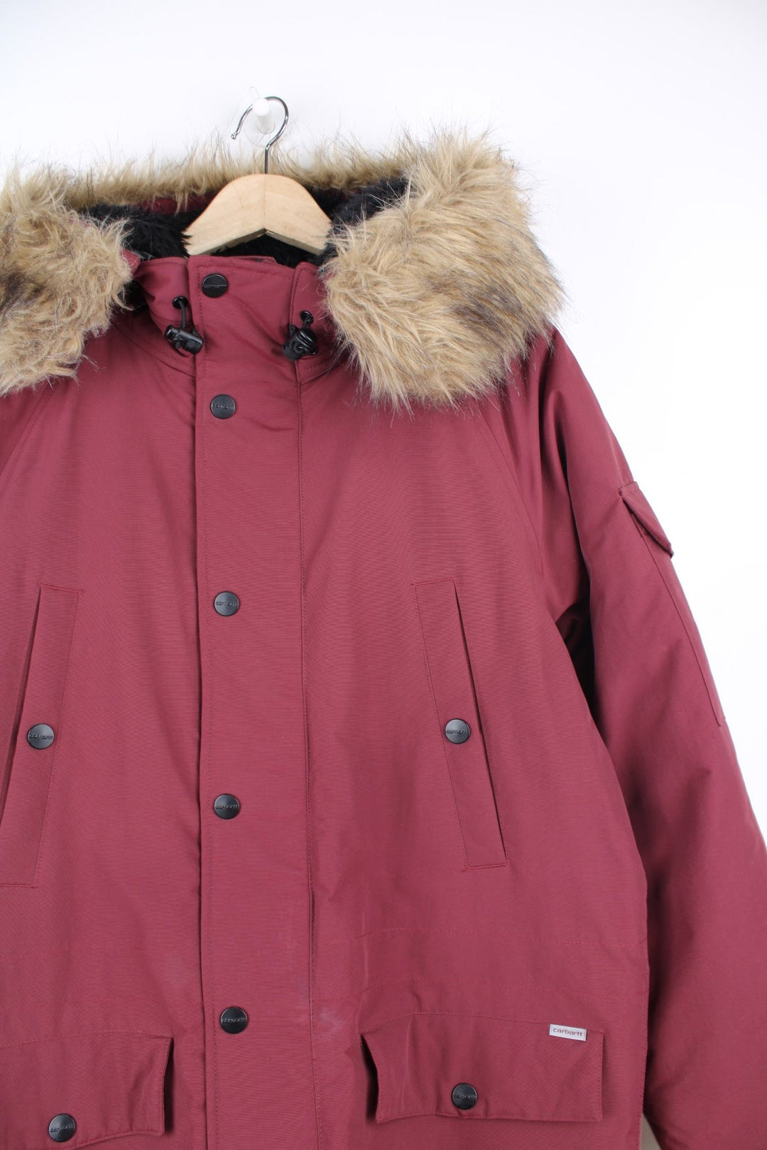 Carhartt Parka Coat in a burgundy colourway, insulated with a quilted lining, has multiple pockets, detachable faux fur hood, and has the logo embroidered on the front and left sleeve.