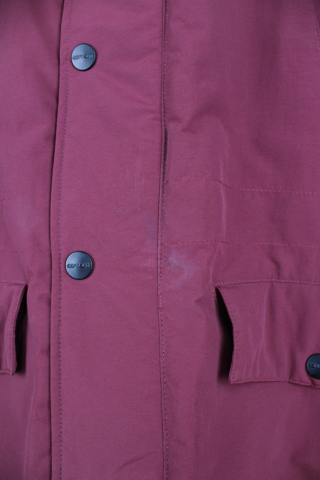 Carhartt Parka Coat in a burgundy colourway, insulated with a quilted lining, has multiple pockets, detachable faux fur hood, and has the logo embroidered on the front and left sleeve.