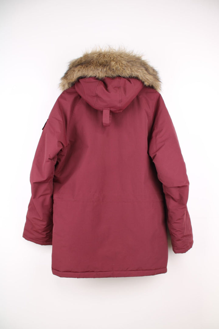 Carhartt Parka Coat in a burgundy colourway, insulated with a quilted lining, has multiple pockets, detachable faux fur hood, and has the logo embroidered on the front and left sleeve.