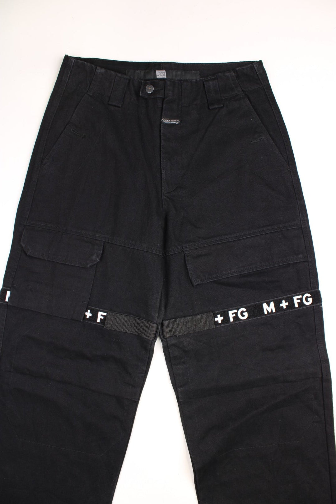 Marithe Francios Girbuad Y2K Trousers in a black colourway with multiple utility style pockets, velcros straps going down the legs with 'M + FG' embroidered on. 