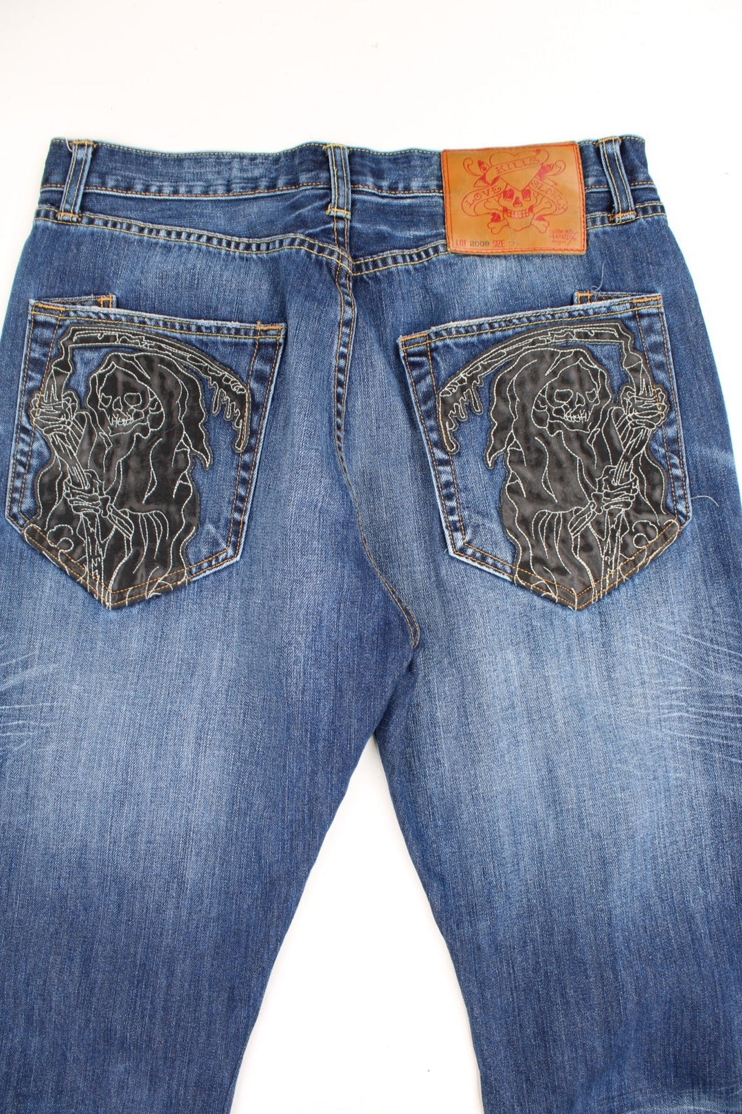 Y2K Ed Hardy faded effect blue denim jeans with embroidered leather skulls on both back pockets and signature Love Kills Slowly leather badge.