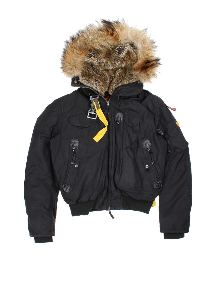 Parajumpers Gobi down coat in black with multiple utility pockets, a velcro logo patch, fur-lined hood, and a PJS carabiner attached.