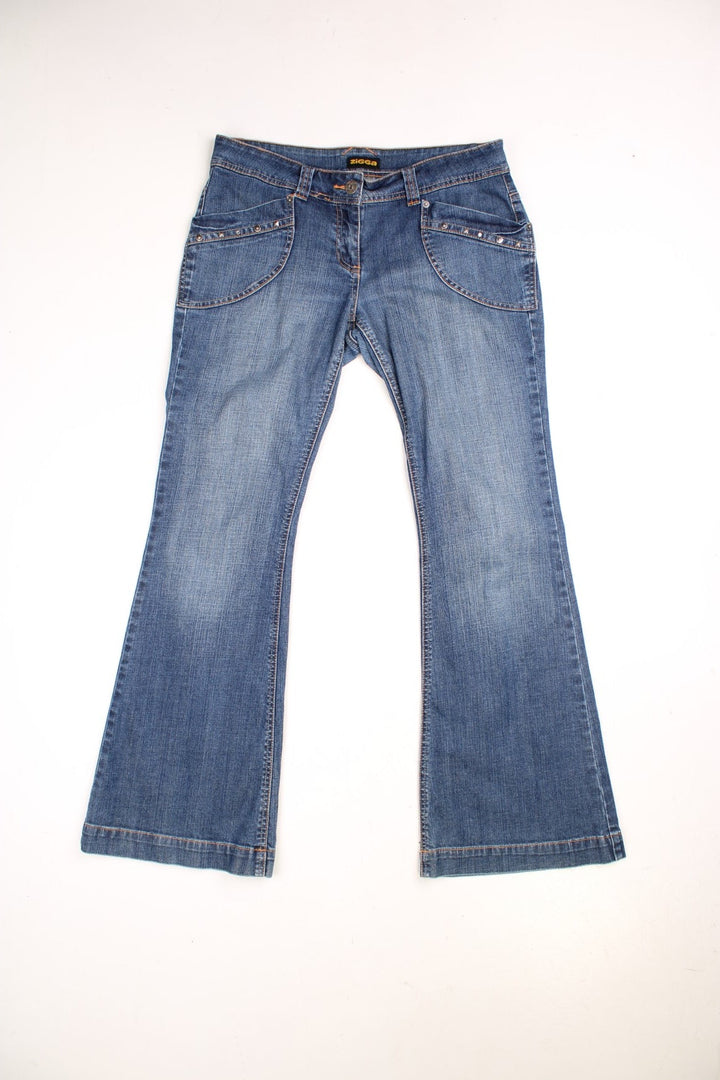 Y2K Flared Zigga jeans in dark blue denim colourway, has pockets with studs embroidered on and contrast stitching on the back pockets.