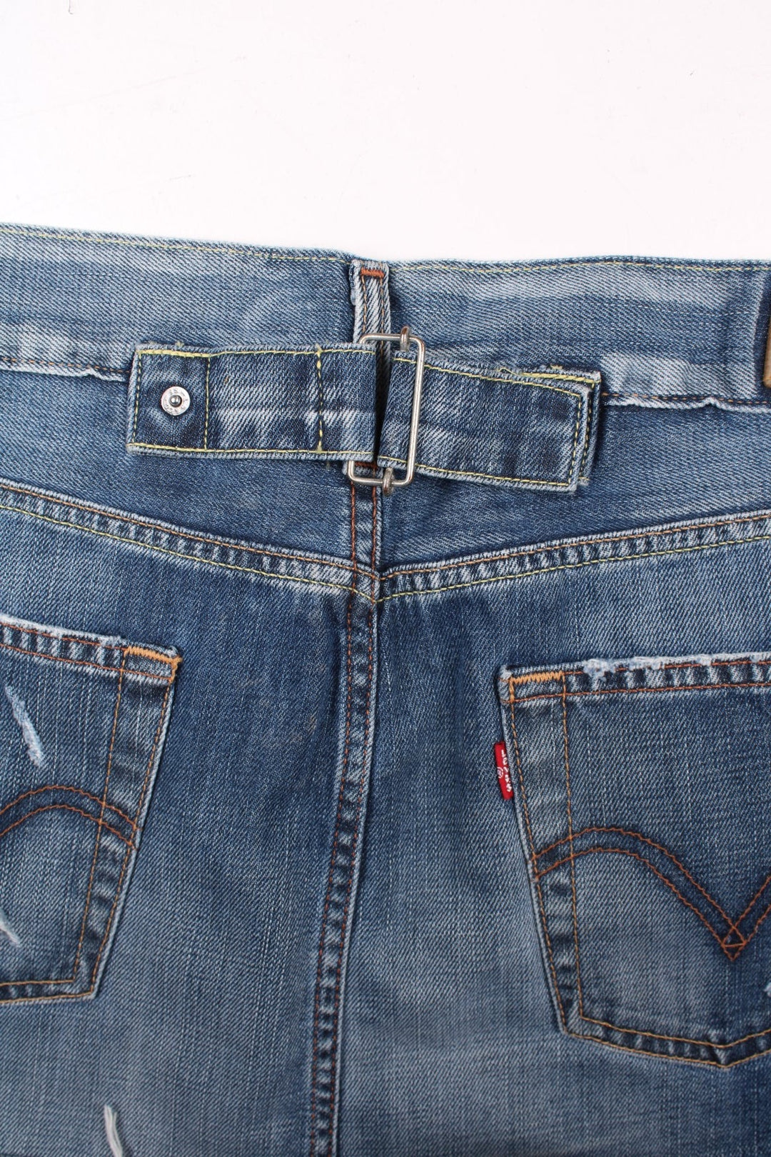 Y2K Levi Strauss denim mini skirt in blue with zip and button closure, four pockets, a raw hem and distressing to pockets, a buckle tightener in the back and a Levi's cowboy patch.