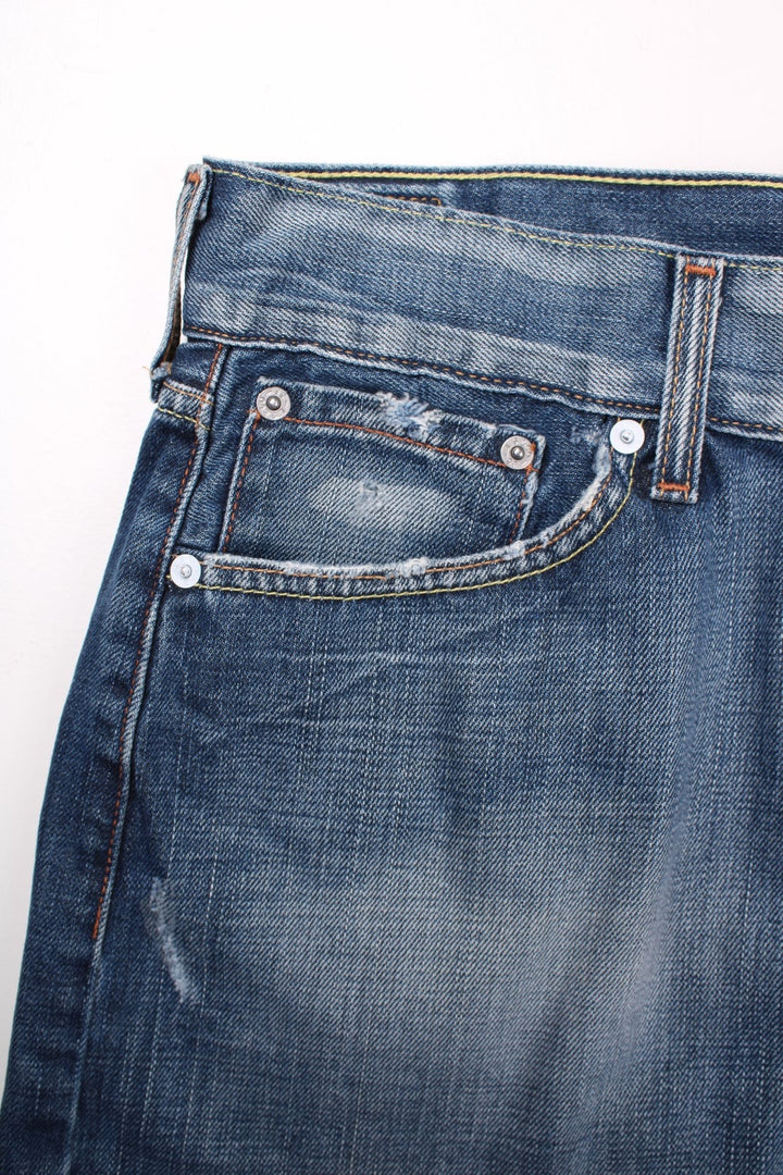 Y2K Levi Strauss denim mini skirt in blue with zip and button closure, four pockets, a raw hem and distressing to pockets, a buckle tightener in the back and a Levi's cowboy patch.