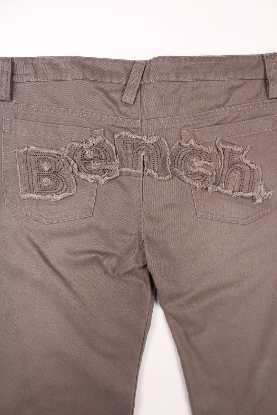 Bench straight leg lightweight trousers in brown with zip and button closure, four pockets, and a distressed embroidered spellout across the back..