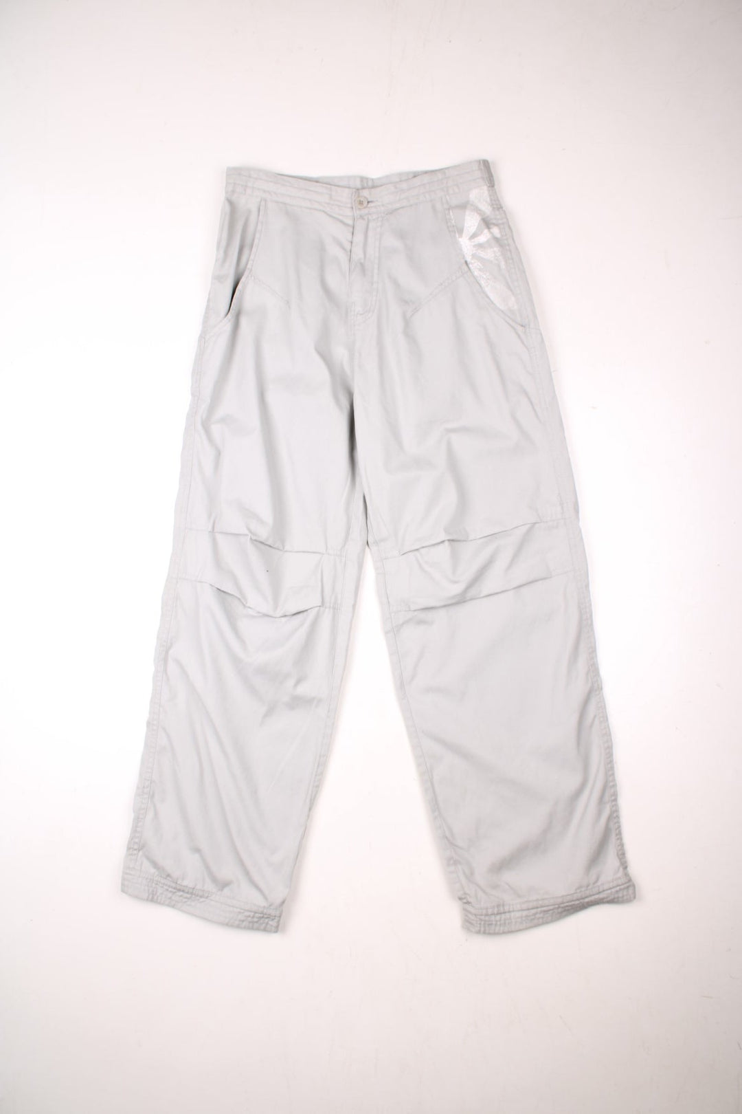 Bench pleated knee cargo pants in tan with four pockets, buttoned adjusters at the waist and printed logos in white above the front left and back right pockets.