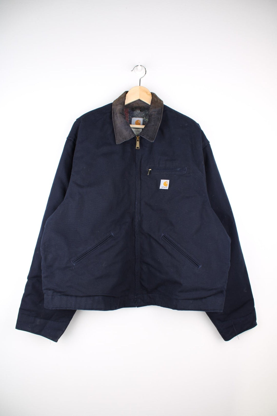 Carhartt Detroit Jacket in a navy blue colourway with a corduroy collar. Zips up and has multiple pockets, insulated with a blanket lining, and has the logos embroidered on the front.