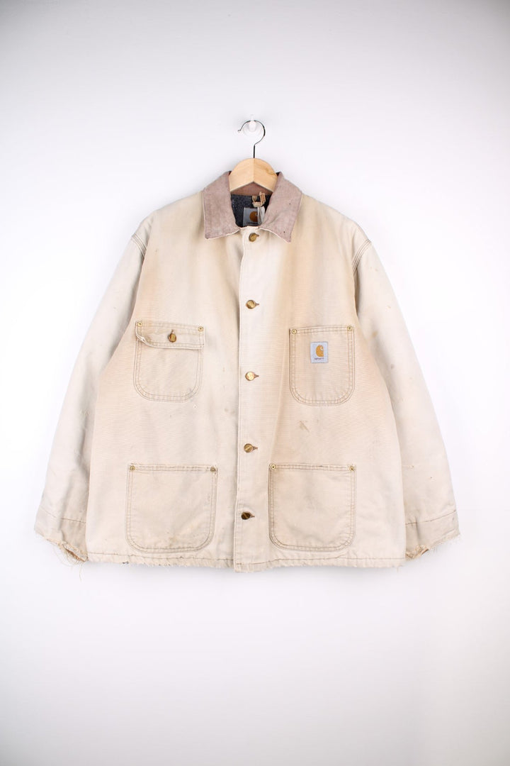 Carhartt Distressed Chore Jacket in a white colourway. Buttons up and has multiple pockets, insulated with a blanket lining, and has the logos embroidered on the front.