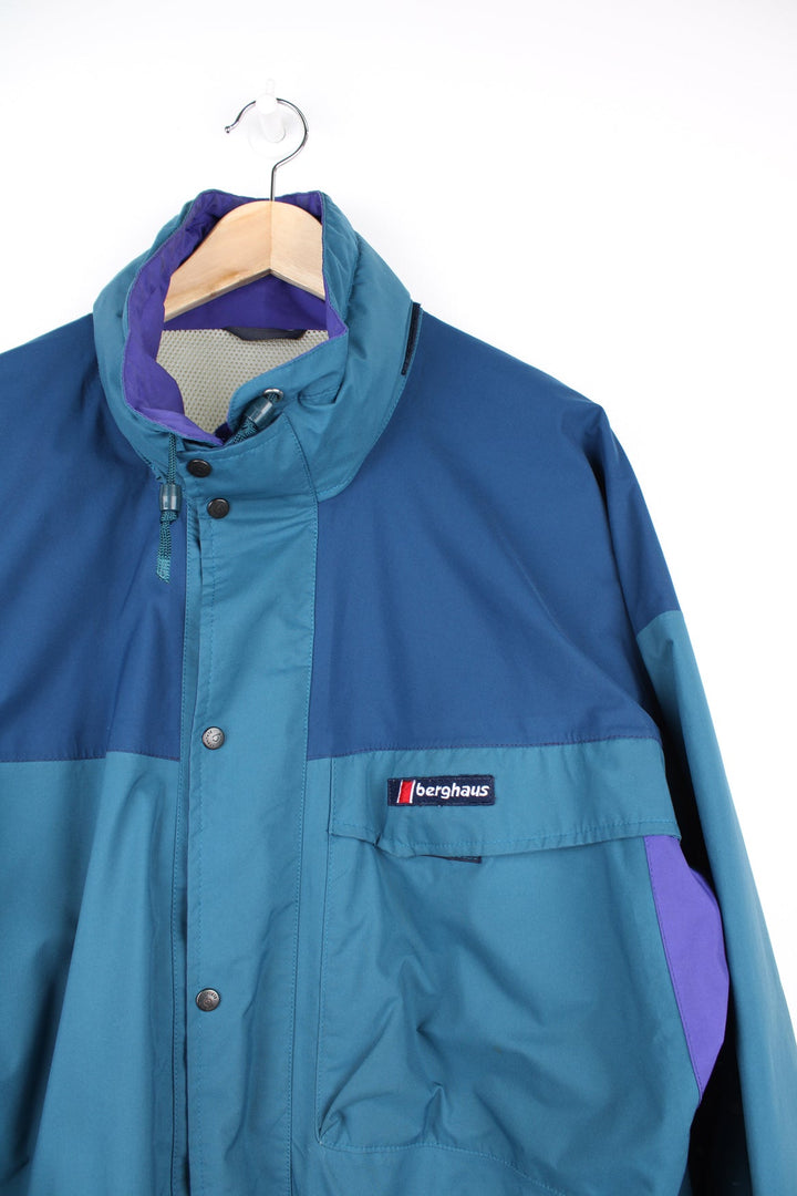 Blue, green and purple Berghaus gore-tex fabric jacket. Features embroidered logo on the chest, drawstring waist and pack away hood.