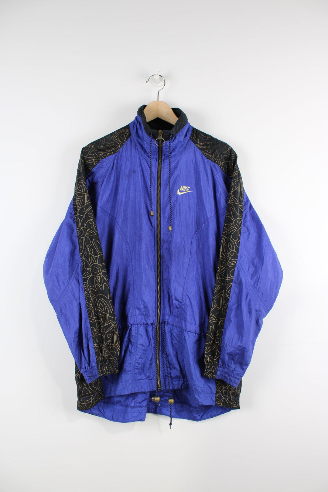 Vintage 90s purple Nike tracksuit jacket. Features a gold embroidered logo on the chest, black panelling with a gold pattern print and a toggle tie waist.