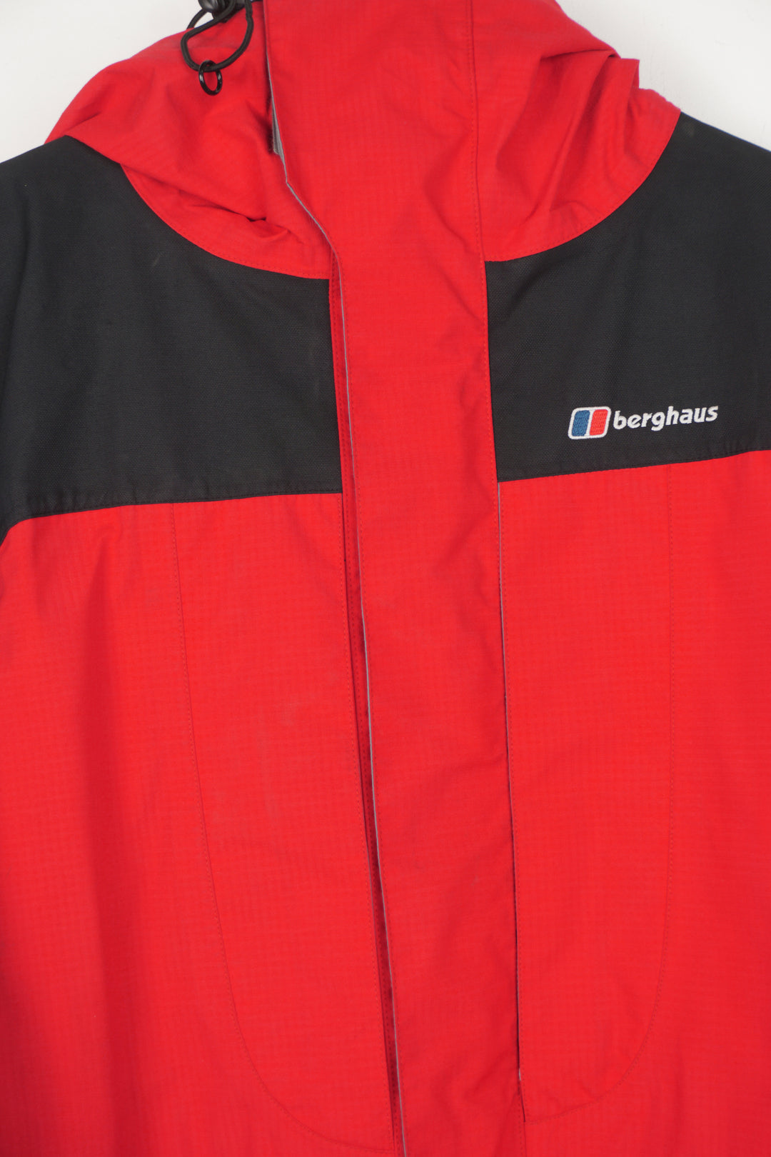 Berghaus red and black zip through waterproof jacket with draw string waist,  embroidered logo on the chest and roll up hood