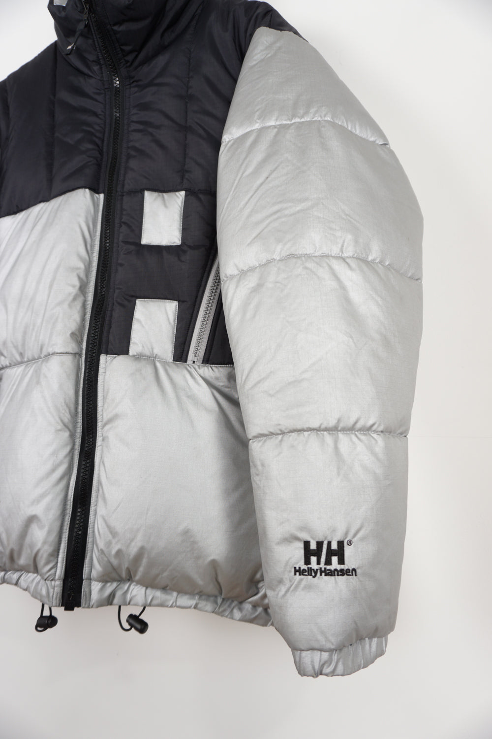 Silver and black Helly Hansen puffer jacket with multiple pockets, drawstring hem and embroidered spell-out logos on front and back